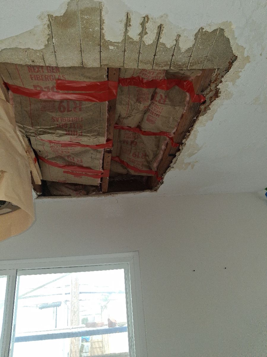 Interior ceiling opening exposing framing and insulation near a window