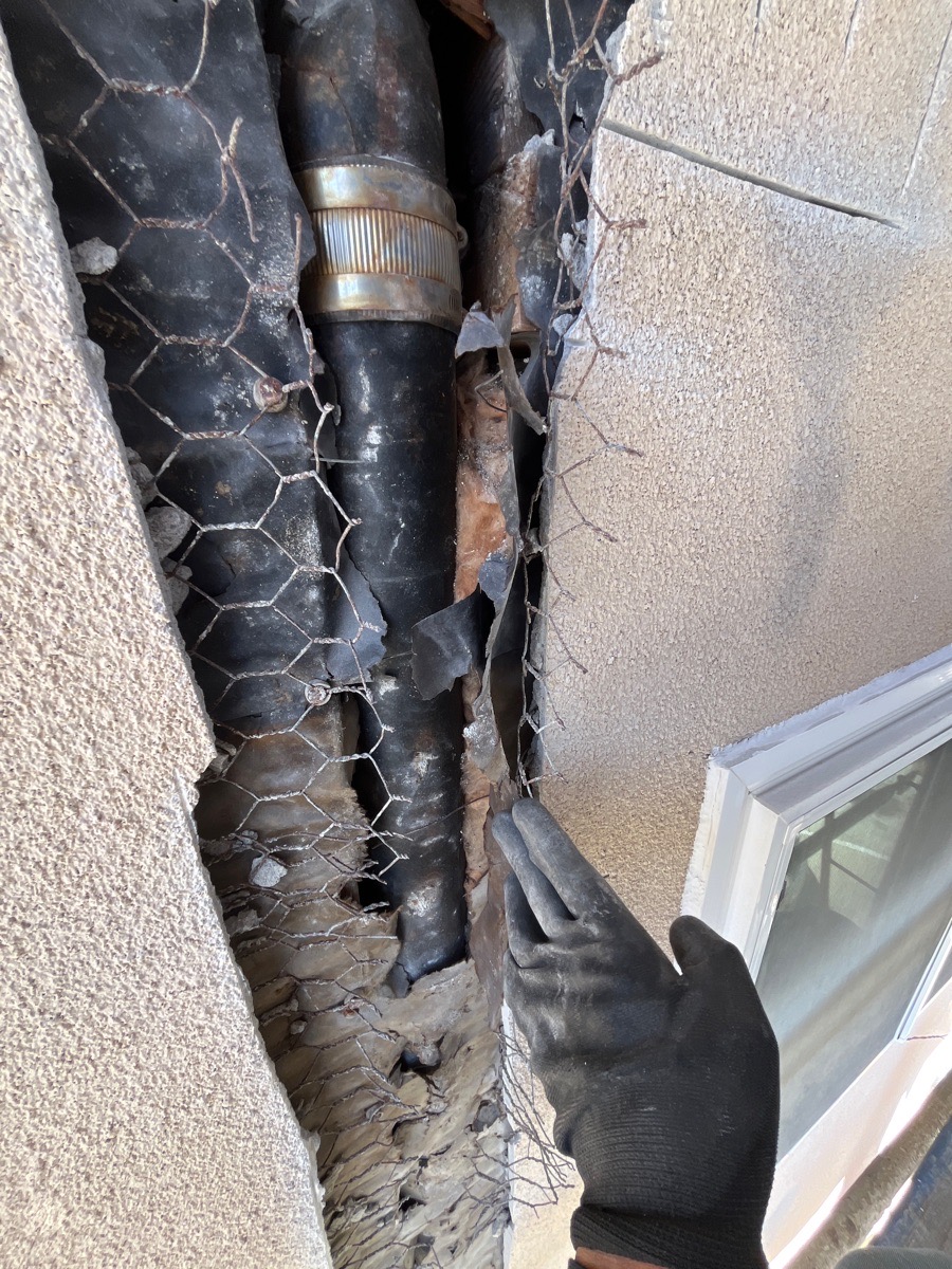 Opened stucco wall exposing pipe and existing lath beside a window